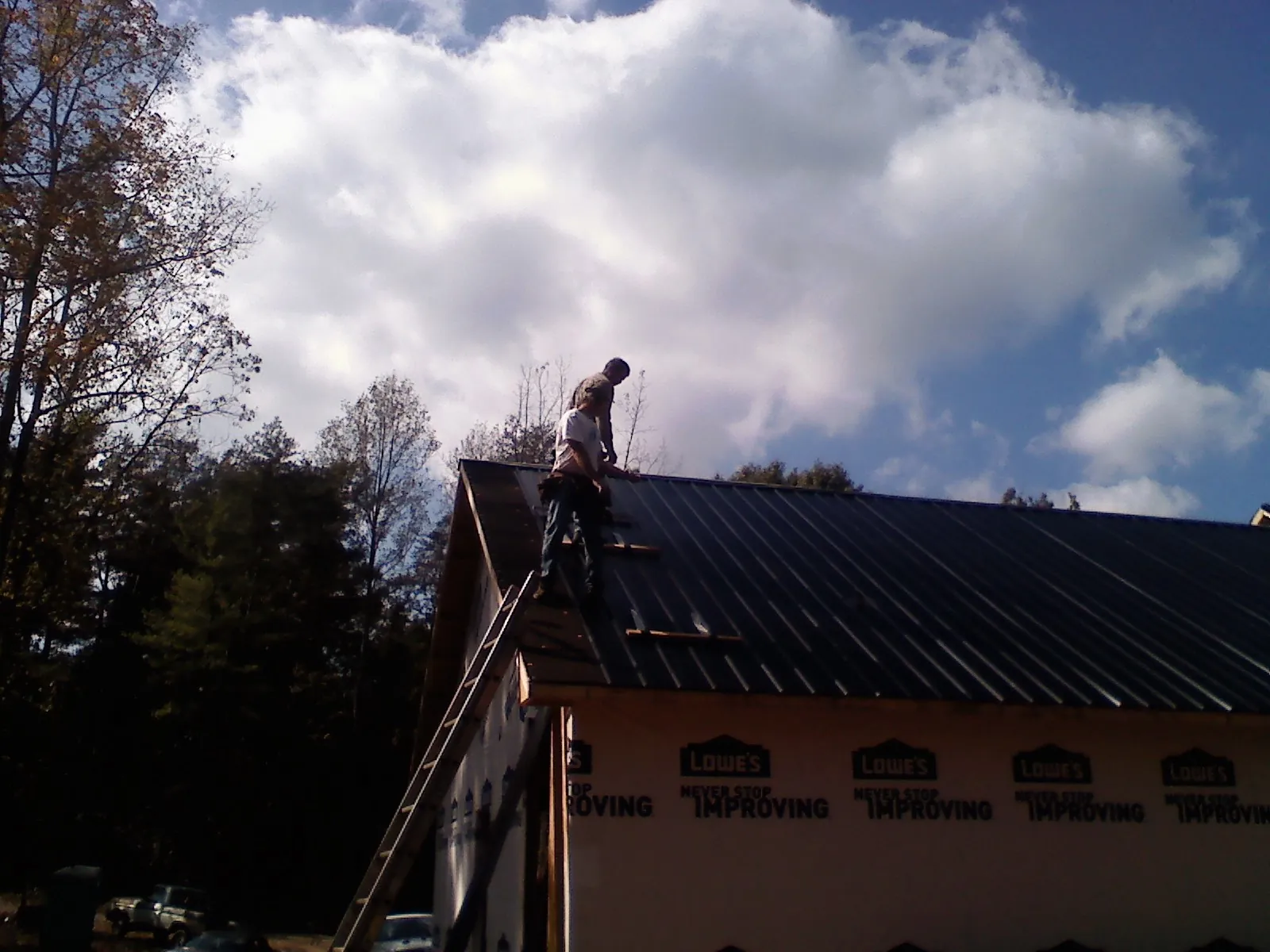 Roofer fastening dark metal panels high against a cloudy sky, from a Roof Inspection job in North Springfield